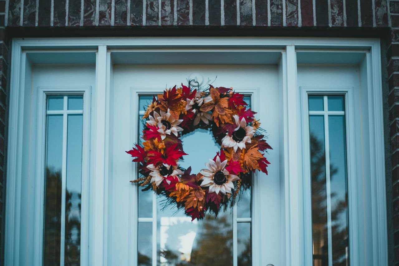 Fall Wreath DIY: Easy Handmade Wreaths for Your Front Door A colorful handmade fall wreath with red, orange, and cream autumn leaves hanging on a light blue front door